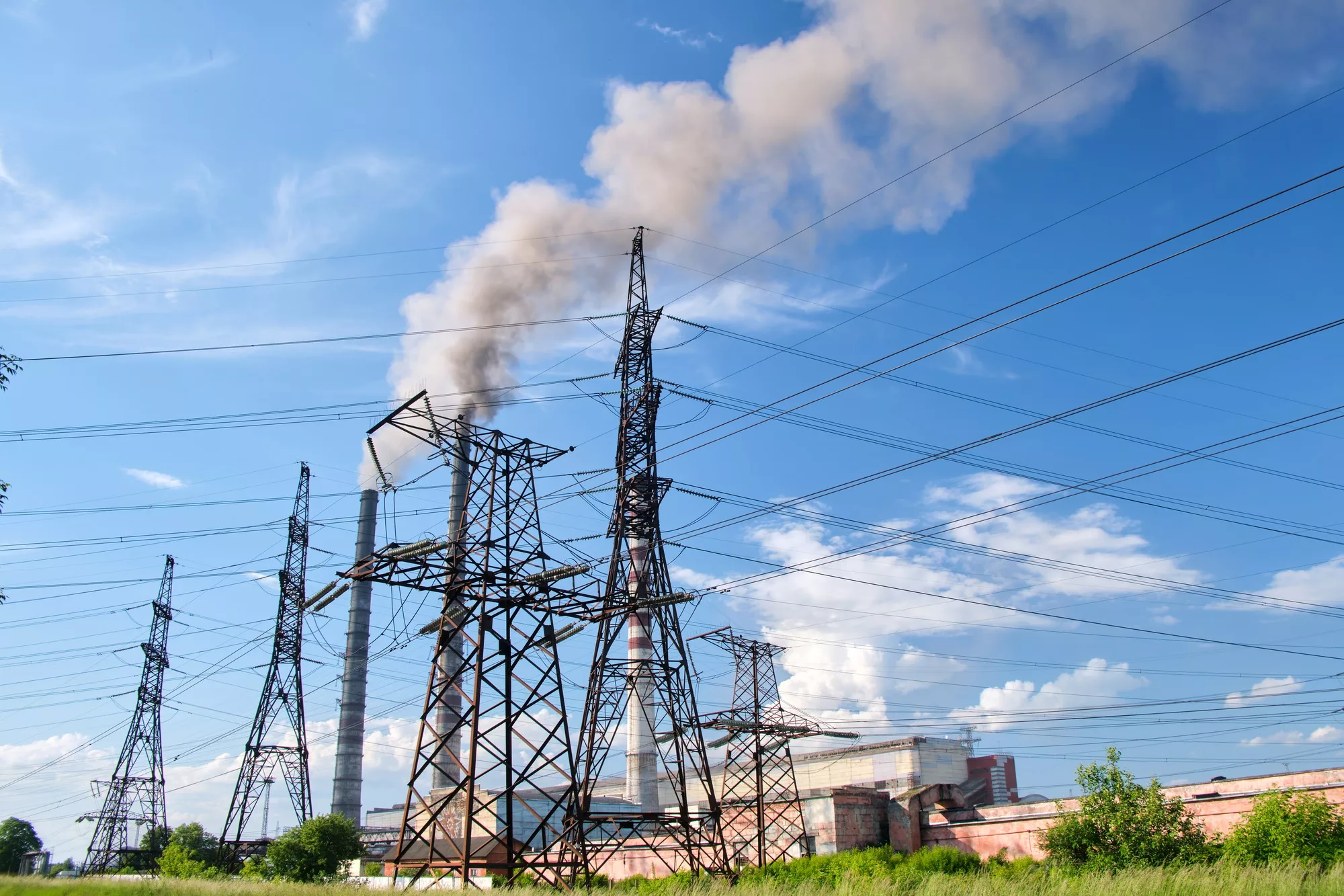 High voltage electric pylons against coal power plant high pipes with black smoke moving upwards