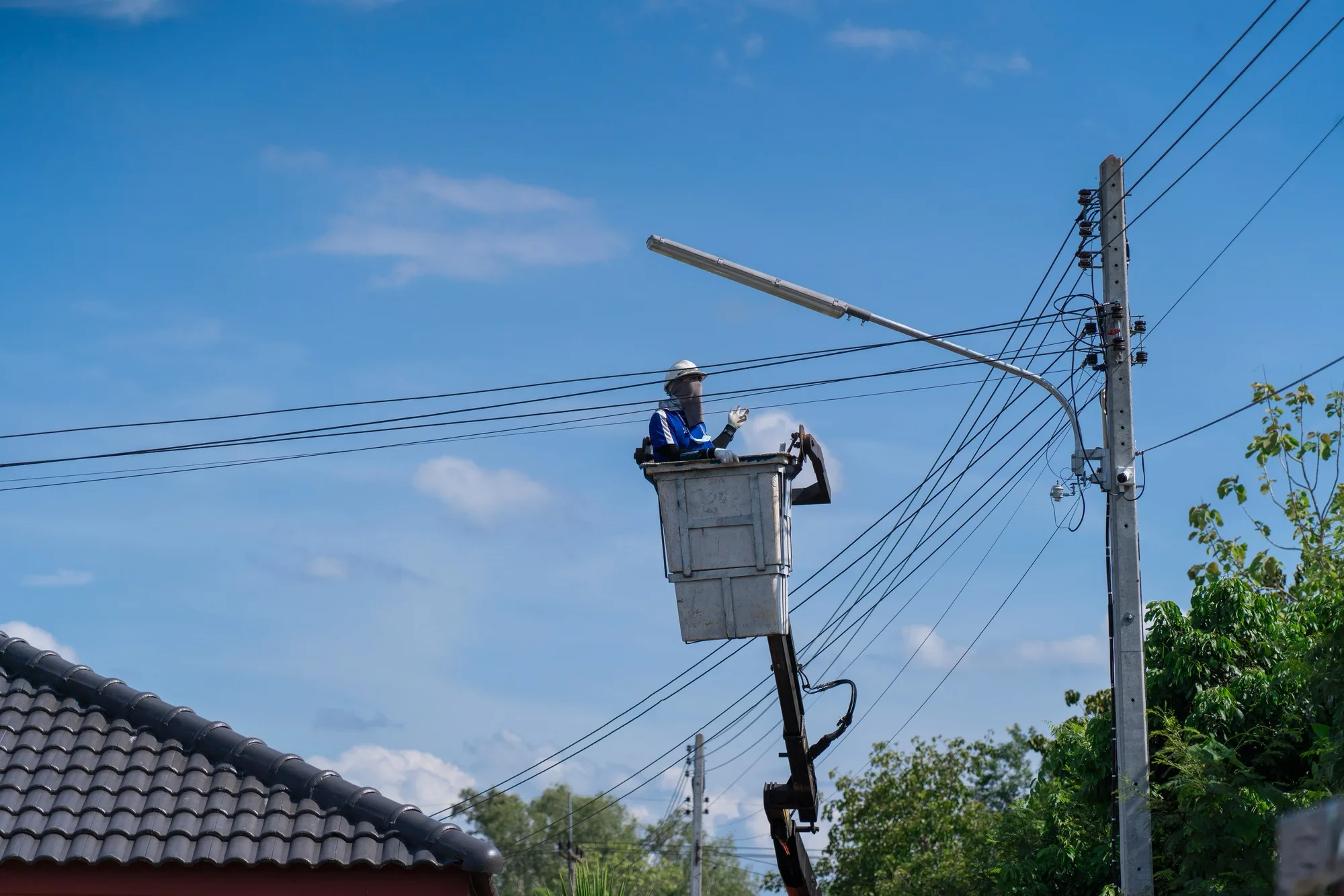 Electrician standing in the basket of a car fixing a lamp at a power pole